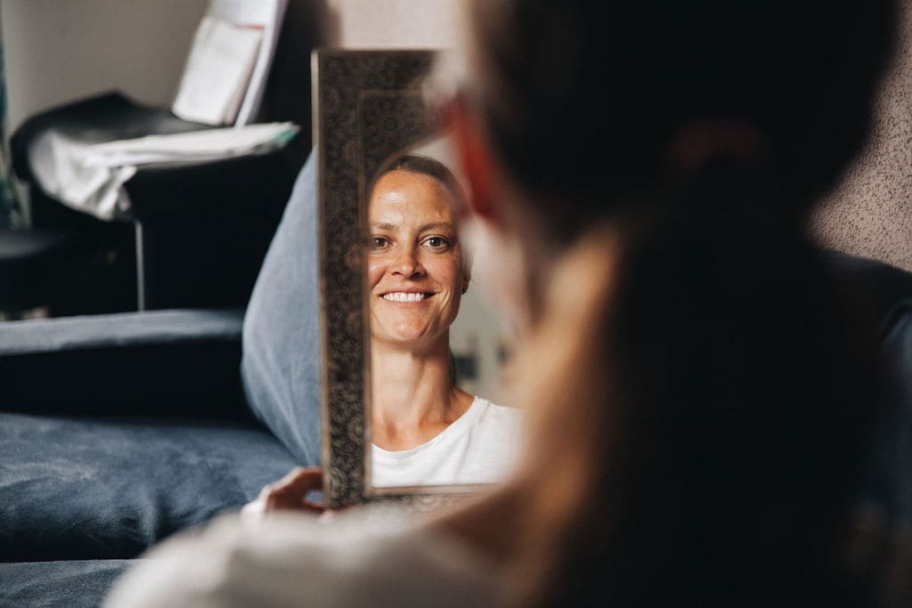 Frau sieht lächelnd in einen Spiegel nachdem sie im Coaching einen Umgang mit ihren negativen Glaubenssätzen gefunden hat