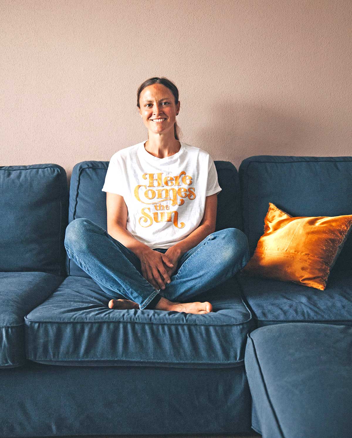 Frau sitzt lächelnd im Schneidersitz auf einer blauen Couch nachdem sie im Coaching einen Umgang mit ihren negativen Gedanken gefunden hat